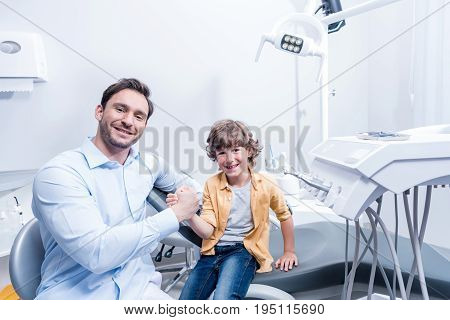 Portrait Of Dentist And Smiling Little Boy Holding Hands In Dental Clinic