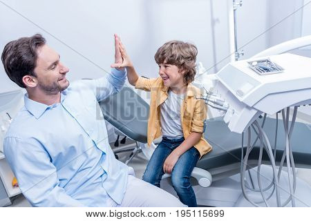 Portrait Of Dentist Giving High Five To Little Boy In Dental Clinic