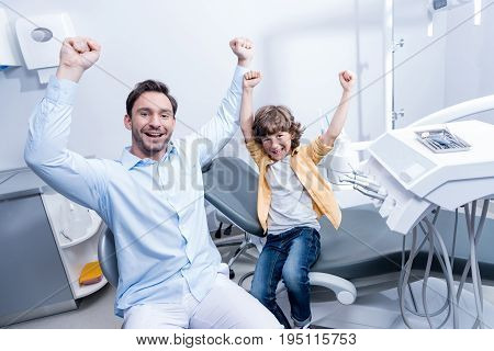 Portrait Of Happy Dentist And Little Boy With Outstretched Arms In Dental Clinic