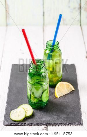 Two botle of infused detox diet refreshing waters: with cucumber and lemon on white wooden table
