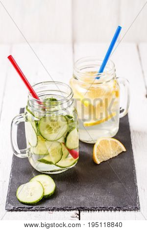 Two mugs of infused detox diet refreshing waters: with cucumber and lemon on white wooden table