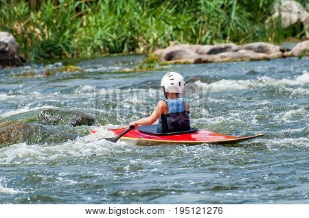 A teenager trains in the art of kayaking. Boat boats on rough river rapids. The child is skillfully engaged in rafting.