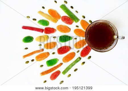 Black tea in a glass cup with colorful pineapple candies and pumpkin seeds on a white background