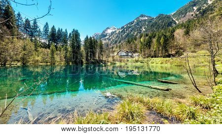Traditional hotel at waterside of clear alpine lake. Snow covered mountains and blue sky.