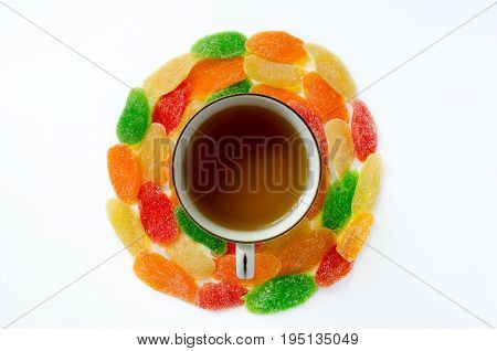 A cup of black tea surrounded by colorful pineapple candied fruits. White background