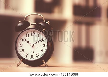 Classic alarm clock showing time during working hours or work break in business office retro toned image with selective focus