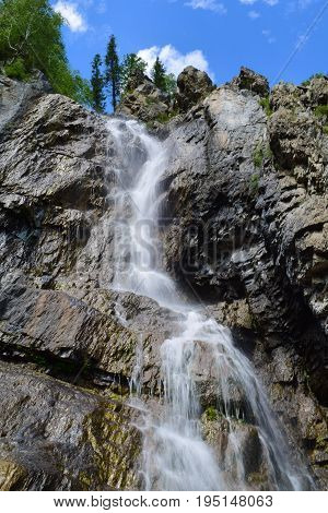 Shirlak waterfall in rocks on blue sky with white clouds background. Tektu river Altai Mountains Altay Republic Siberia Russia. Vertical orientation.