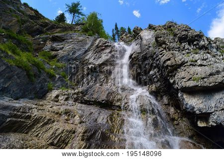Shirlak waterfall in rocks on blue sky with white clouds background. Tektu river Altai Mountains Altay Republic Siberia Russia.