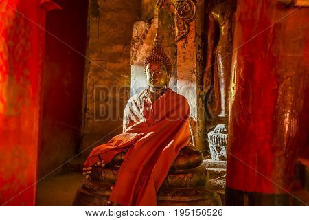 Old Buddha statue wearing yellow robe in light and shadow in old church in Mae Chaem Buddhist temple of Chiangmai Thailand