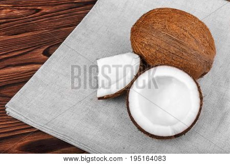 Close-up tasteful coconuts on a dark wooden background. Healthful coconut on a bright gray piece of cloth. Delicious natural ingredients. Exotic tropical nuts.