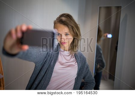 Young woman shopping in a fashion store, trying on some clothes she likes  - taking a selfie picture with her smartphone in the cabin (color toned image; shallow DOF)
