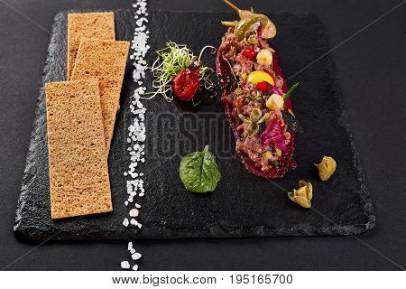 fresh beef tartar with salt and herbs and Crispbread, studio shot. Meat tartar on black shale. Top view