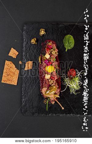 fresh beef tartar with salt and herbs and Crispbread, studio shot. Meat tartar on black shale. Top view