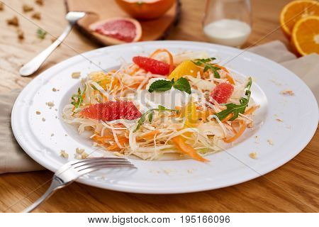 Fresh healthy salad with cabbage, carrot, citrus and yogurt. Vegetable and fruit salad in wwhite plate on wood background.