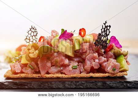 fresh tuna tartar with salt and herbs, studio shot. Fish tartar on black shale. Close-up