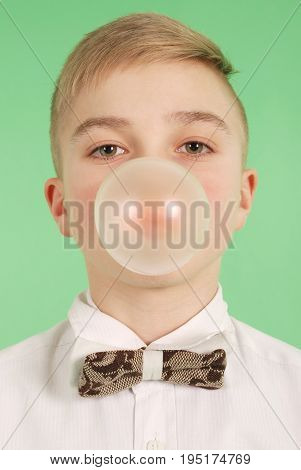 Boy blowing a bubblegum bubble isolated on green