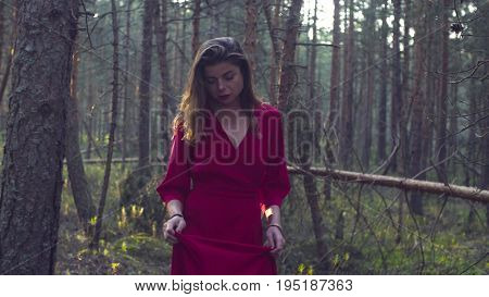 Dolly shot of young beautiful woman in a long red dress walking in the forest
