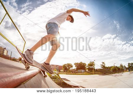 Teenager skater in a cap and shorts on rails on a skateboard in a skate park Wide angle