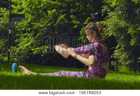 Young woman doing yoga exercises in the park. Akarna Dhanurasana