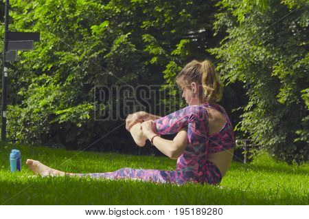 Young woman doing yoga exercises in the park. Akarna Dhanurasana