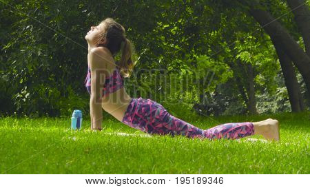 Young woman doing yoga exercises in the park. Artha mukha svanasana