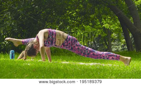 Young woman doing yoga exercises in the park. Artha mukha svanasana