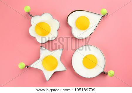 Fried sunny side up eggs in molds of different shapes on color background