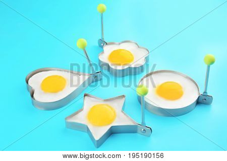 Fried sunny side up eggs in molds of different shapes on color background