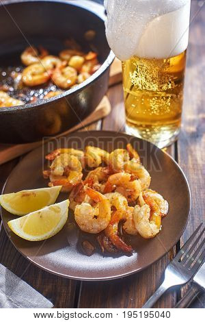 Rustic still life with shrimps in plate next to glass of beer on wooden table. Vertical shot.S