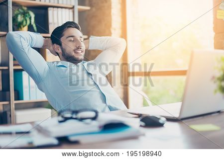 Well Done! Young Cheerful Middle Eastern Guy Realtor Is Resting At A Workplace, Smiling And Enjoying