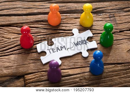 Closeup of teamwork jigsaw pieces surrounded by colorful pawn figurines on wood