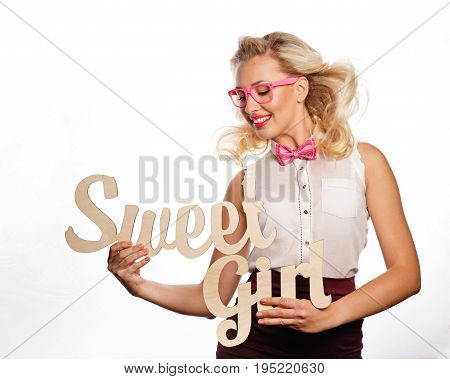 Young attractive girl holding an inscription of a sweet girl. She is wearing a blouse a bow tie and glasses.