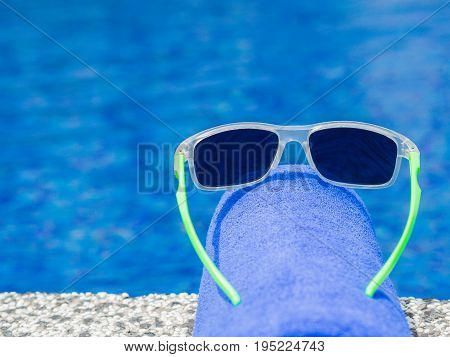 Sunglesses and blue towel at the side of swimming pool. Vacation beach summer travel concept