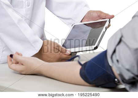 Female patient getting checkup with a doctor using a modern electronic blood pressure monitor. The device is a smart medical gadget and connects to a tablet. The diagnosis is made possible by health insurance.