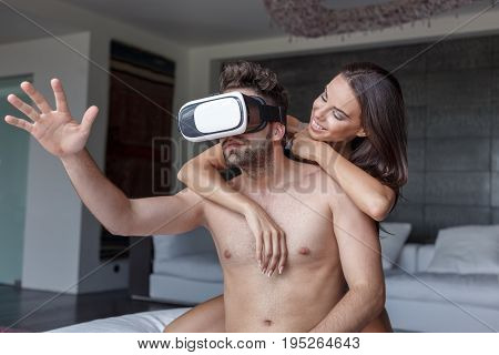 Young man with VR headset and girlfriend playing virtual reality at home