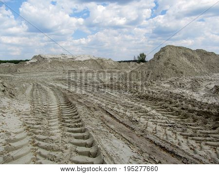 Sandy quarry with prints of tires of the tippers and a beautiful sky in the clouds above it. Heaps of white industrial sand and gentle blue sky above them
