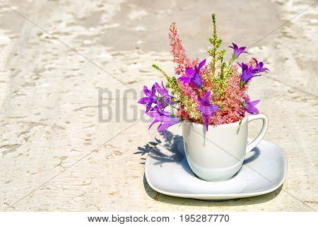 Astilba and blue bell flowers bouquet in a white coffee cup on an old white background with copy space for your text