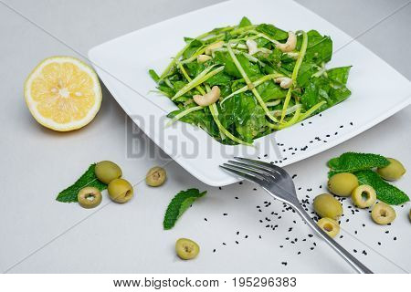 Fresh salad with lemon. Fresh spinach salad with lemon and nuts on a white background on a white plate top view.