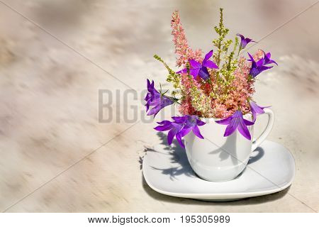 astilba and bluebell bouquet in a coffee cup as a vase on a light brown background with copy space for your text