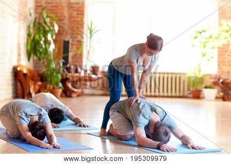 fitness, sport and healthy lifestyle concept - group of people with personal trainer doing yoga hare pose on mats in gym or studio