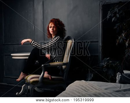 Ginger girl sitting at home on the design chair next to the table