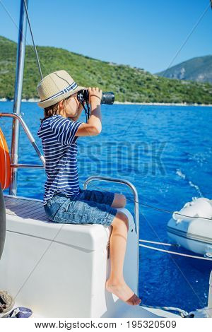 Cute boy captain on board of sailing yacht on summer cruise. Travel adventure, yachting with child on family vacation. Kid clothing in sailor style, nautical fashion.