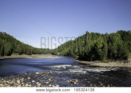 Ljungan River in Sweden with forest and a clear blue sky.
