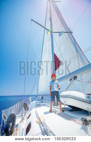 Cute boy captain on board of sailing yacht on summer cruise. Travel adventure, yachting with child on family vacation. Kid clothing in sailor style, nautical fashion.