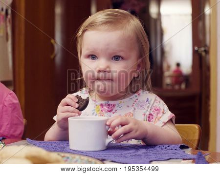 Little baby girl eating cookies and drinking tea