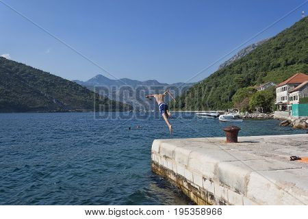LEPETANI MONTENEGRO - JUNE 27 2017: An unknown young man jumps into the water from a pier near the village of Lepetani