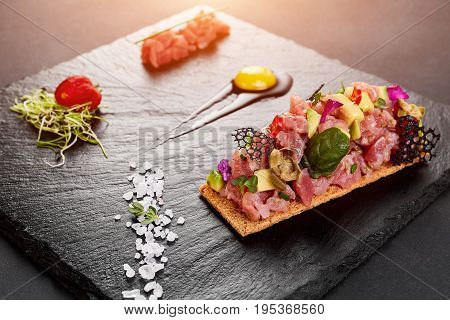 fresh tuna tartar with salt and herbs, studio shot. Fish tartar on black shale. Close-up