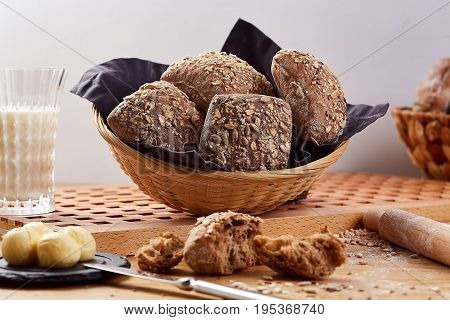 Baked basket with rye buns on wooden table. Rye bread with seeds and glass of milk, close-up.