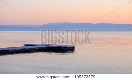 View on the sunrise on the sea the mountains and a wooden pier on the beach Moraitika island Corfu Greece.