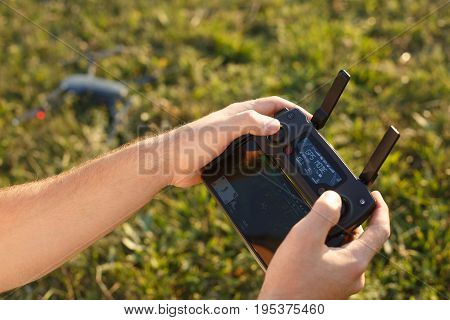 Man holds a drone remote controller in his hands. Quadcopter is on the ground ready to go and fly blurred on the background. No face